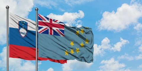 Slovenia and Tuvalu flag waving in the wind against white cloudy blue sky together. Diplomacy...