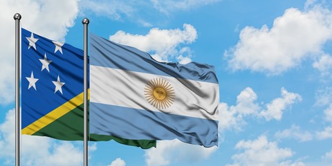 Solomon Islands and Argentina flag waving in the wind against white cloudy blue sky together....