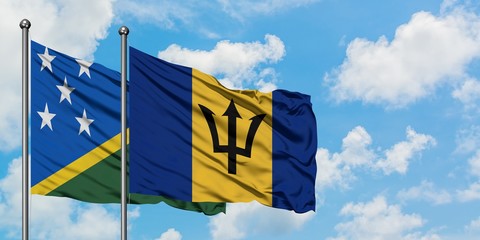 Solomon Islands and Barbados flag waving in the wind against white cloudy blue sky together. Diplomacy concept, international relations.