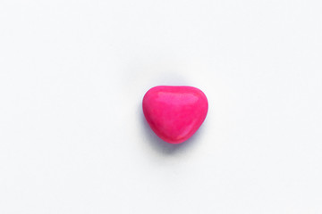 Small heart-shaped candy made of milk chocolate covered with raspberry glaze on a white background