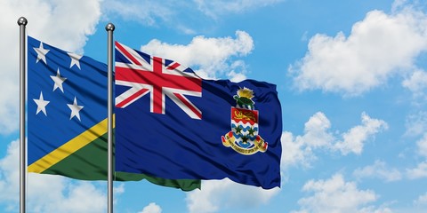Solomon Islands and Cayman Islands flag waving in the wind against white cloudy blue sky together....