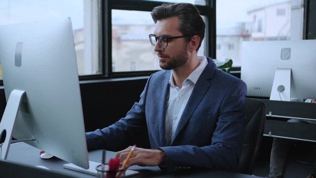 Confident caucasian entrepreneur keyboarding on desktop computer managing business technology working tasts in modern office.