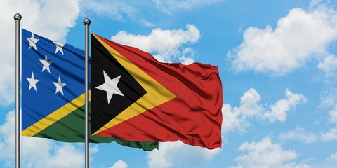 Solomon Islands and East Timor flag waving in the wind against white cloudy blue sky together....