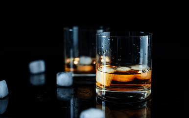 Two elegant simple glass of luxury whisky with ice cubes against black background