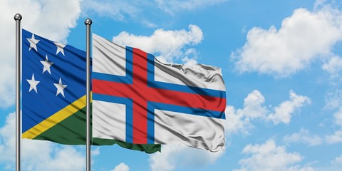 Solomon Islands and Faroe Islands flag waving in the wind against white cloudy blue sky together....