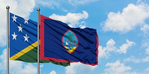 Solomon Islands and Guam flag waving in the wind against white cloudy blue sky together. Diplomacy concept, international relations.