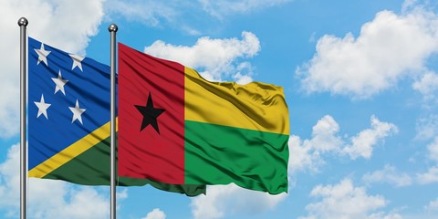 Solomon Islands and Guinea Bissau flag waving in the wind against white cloudy blue sky together....