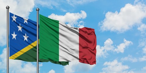Solomon Islands and Italy flag waving in the wind against white cloudy blue sky together. Diplomacy...