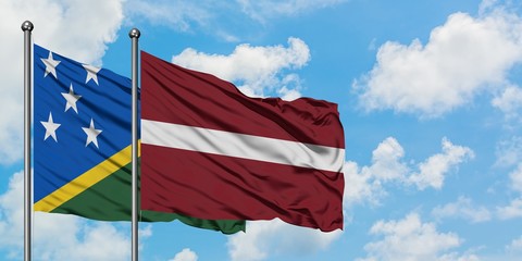 Solomon Islands and Latvia flag waving in the wind against white cloudy blue sky together....