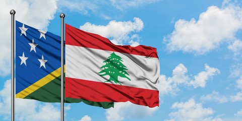 Solomon Islands and Lebanon flag waving in the wind against white cloudy blue sky together....