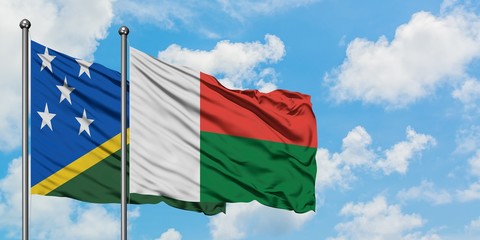 Solomon Islands and Madagascar flag waving in the wind against white cloudy blue sky together. Diplomacy concept, international relations.