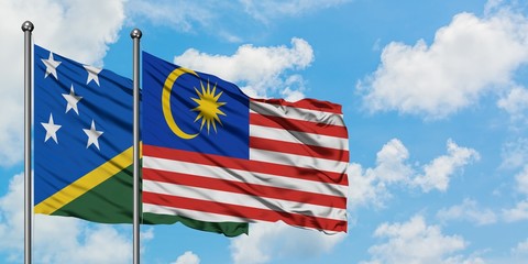 Solomon Islands and Malaysia flag waving in the wind against white cloudy blue sky together. Diplomacy concept, international relations.