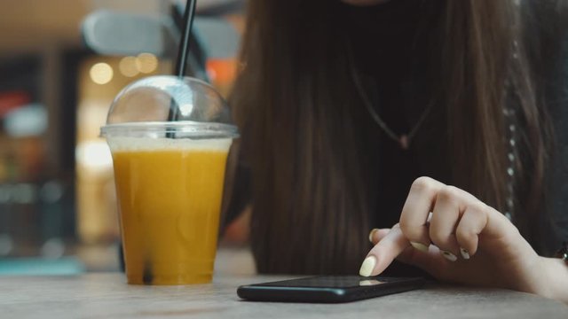 Young woman browsing on smartphone in cafe on wooden table, drinking juce. Businesswoman typing on mobile phone. 4K UHD
