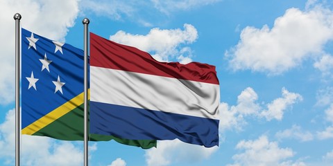 Solomon Islands and Netherlands flag waving in the wind against white cloudy blue sky together....