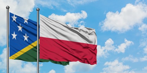 Solomon Islands and Poland flag waving in the wind against white cloudy blue sky together....