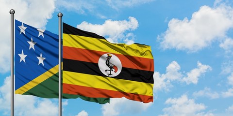 Solomon Islands and Uganda flag waving in the wind against white cloudy blue sky together. Diplomacy concept, international relations.