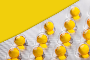 Metal drug blister with yellow medicine capsules. Vibrant color cure in transparent silver container. Healthcare medication pharmacy background.