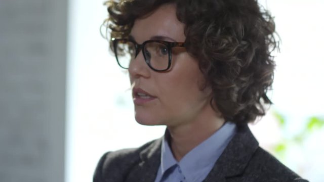 Tilt Up Of Serious Young Woman With Short Curly Hair Wearing Glasses And Talking To Someone Off Camera