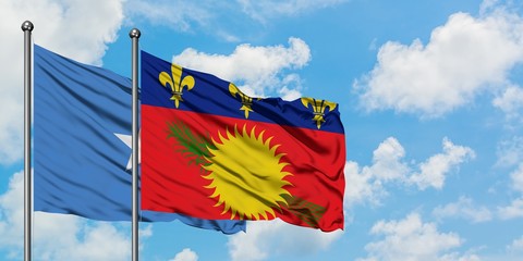 Somalia and Guadeloupe flag waving in the wind against white cloudy blue sky together. Diplomacy...