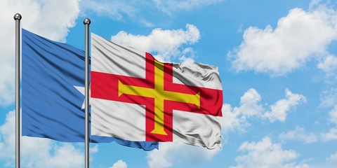 Somalia and Guernsey flag waving in the wind against white cloudy blue sky together. Diplomacy concept, international relations.