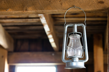 Old fashioned vintage kerosene oil lantern lamp burning with a soft glow light in an antique rustic country barn with aged wood wall and weathered wooden floor