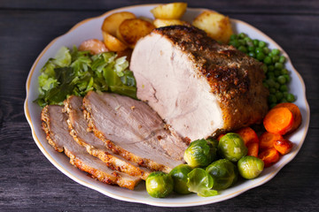 Roasted sliced ham and vegetables: potatoes, carrots, brussel sprouts, cabbage and green peas on...