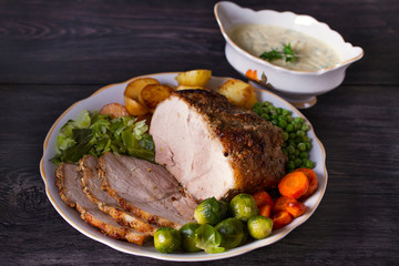 Roasted sliced ham and vegetables: potatoes, carrots, brussel sprouts, cabbage and green peas on black wooden background