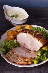 Roasted sliced ham and vegetables: potatoes, carrots, brussel sprouts, cabbage and green peas on black wooden background