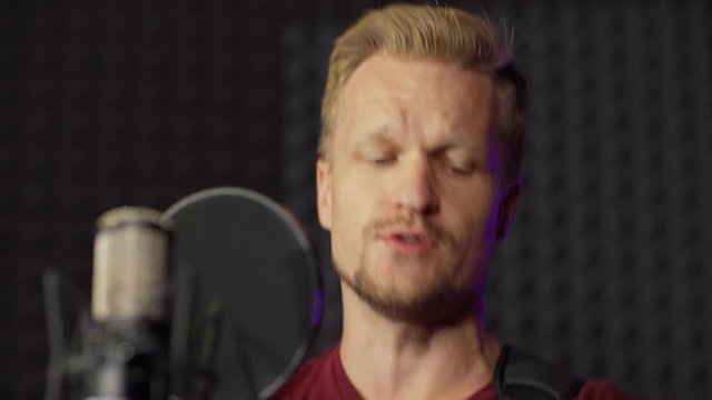 Middle Aged Male Artist Playing Guitar And Singing In Microphone Standing In Music Recording Studio Booth, Closeup Tilt Up Shot