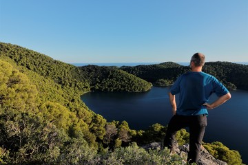 hiker standing on top of a mountain with stunning panoramic  view to green hills and blue lake