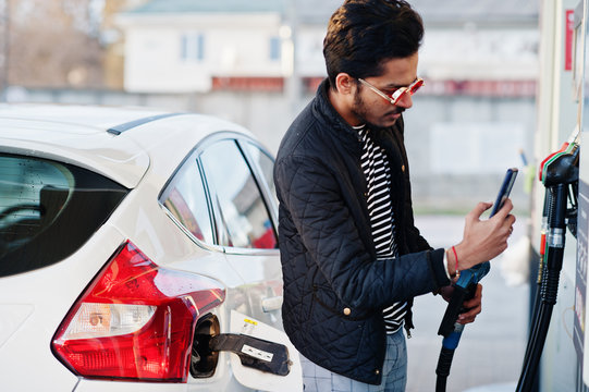 South Asian Man Or Indian Male Refueling His White Car On Gas Station And Pay By Mobile Phone.