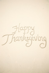 Happy Thanksgiving travel message handwritten in careful calligraphy script on smooth light sand beach