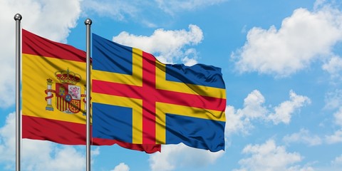 Spain and Aland Islands flag waving in the wind against white cloudy blue sky together. Diplomacy...