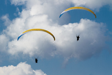 Two paragliders in flight with puffy clouds in the background