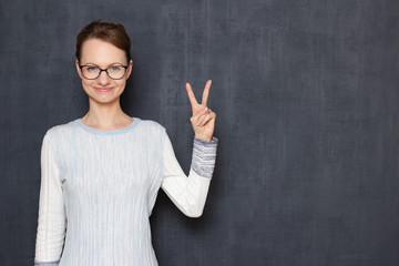 Portrait of happy girl with glasses, showing victory gesture