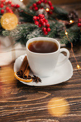 Black tea in a white cup with a saucer on a wooden table, spruce branch and light textile in the background. Winter tea