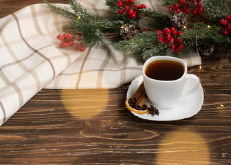 Black tea in a white cup with a saucer on a wooden table, spruce branch and light textile in the...