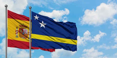 Spain and Curacao flag waving in the wind against white cloudy blue sky together. Diplomacy concept, international relations.