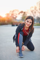Young modern woman tying running shoes in urban park. © astrosystem