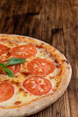 Close up of classic italian Margherita with melted cheese and tomatoes on wooden rustic table