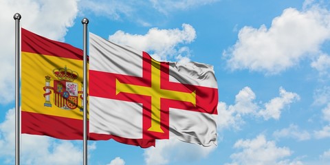 Spain and Guernsey flag waving in the wind against white cloudy blue sky together. Diplomacy concept, international relations.