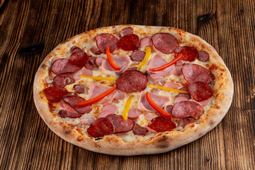 Mixed meat pizza with pepperoni, chorizo, ham, sausages and bell pepper with melted cheese on wooden table