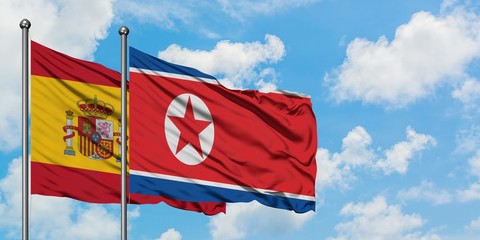 Spain and North Korea flag waving in the wind against white cloudy blue sky together. Diplomacy...