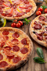 Top view of various assorted pizzas on rustic wooden table with ingredients on it