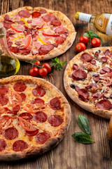 Top view of various assorted pizzas on rustic wooden table with ingredients on it