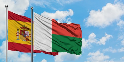Spain and Madagascar flag waving in the wind against white cloudy blue sky together. Diplomacy...