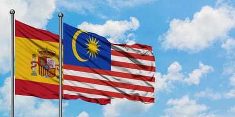 Spain and Malaysia flag waving in the wind against white cloudy blue sky together. Diplomacy concept, international relations.