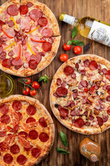 Top view of various assorted pizzas on rustic wooden table with ingredients on it