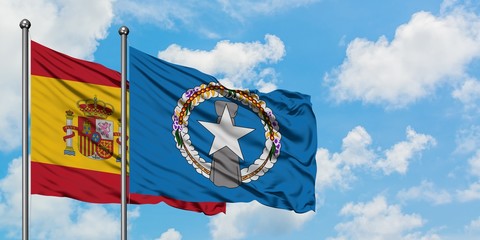 Spain and Northern Mariana Islands flag waving in the wind against white cloudy blue sky together....
