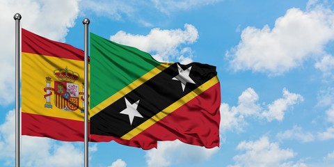 Spain and Saint Kitts And Nevis flag waving in the wind against white cloudy blue sky together. Diplomacy concept, international relations.